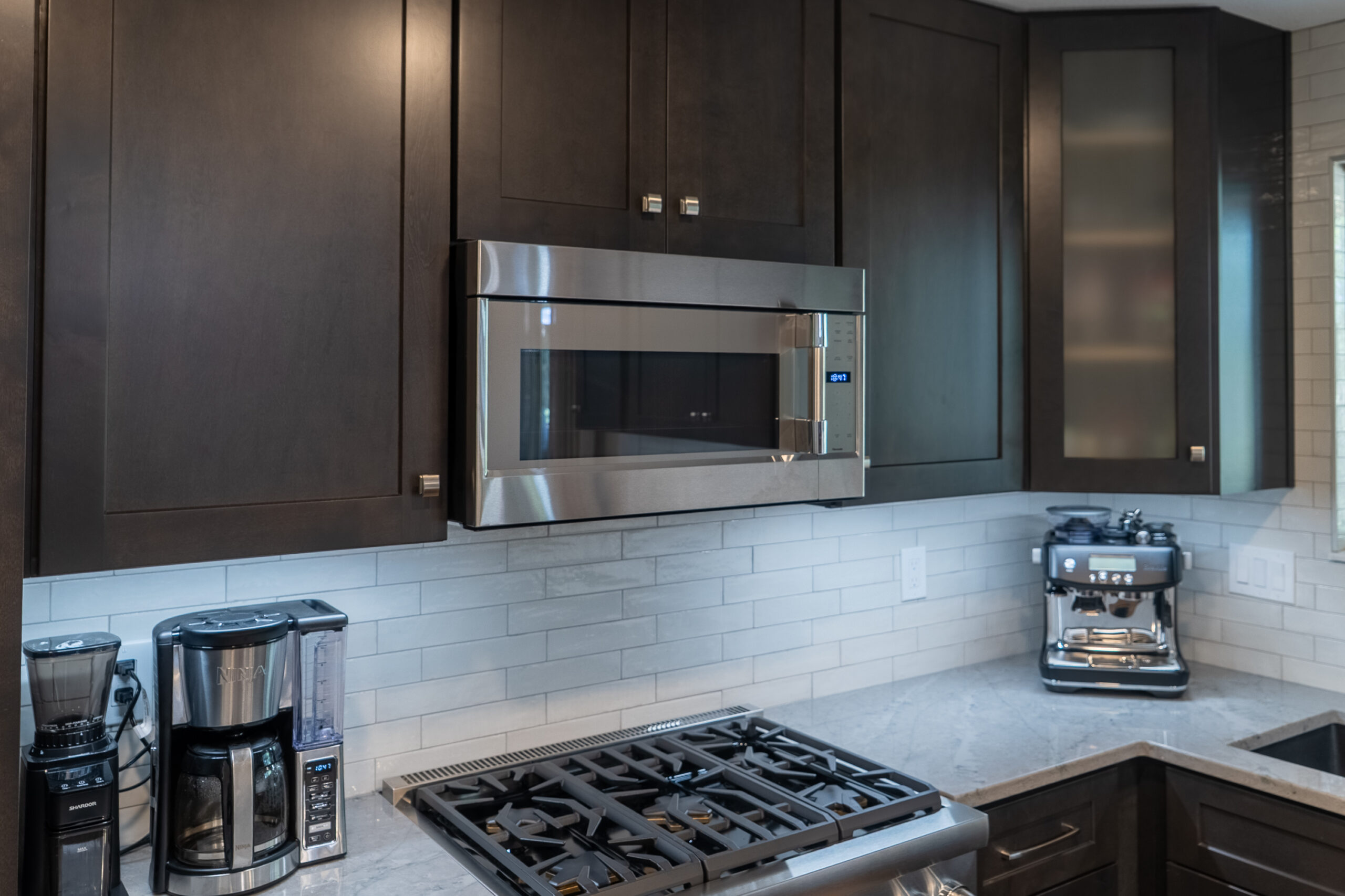 Modern kitchen with stainless steel microwave and stove under dark wood cabinets.